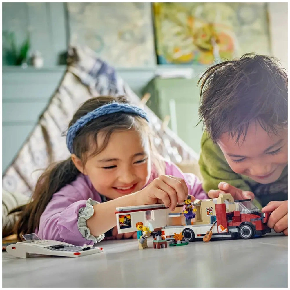 Two children joyfully playing with the LEGO® City Holiday Adventure Camper Van set, assembling figures and accessories on a wooden floor.