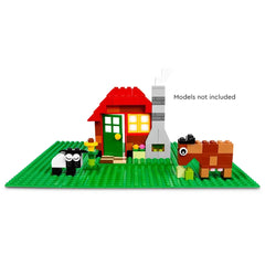 LEGO Classic Green Baseplate featuring a colorful toy house with a red roof, green door, and a stone chimney. Two playful animals, a black and white sheep and a brown horse, are visible on the lush green baseplate, surrounded by colorful flowers and greenery.