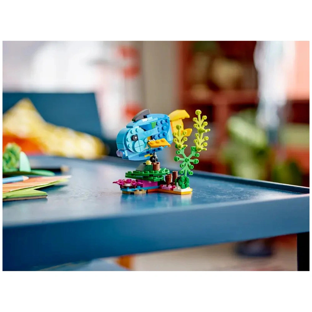 Colorful LEGO Creator 3in1 fish construction set displayed on a blue table, surrounded by vibrant plant pieces, capturing an underwater scene.