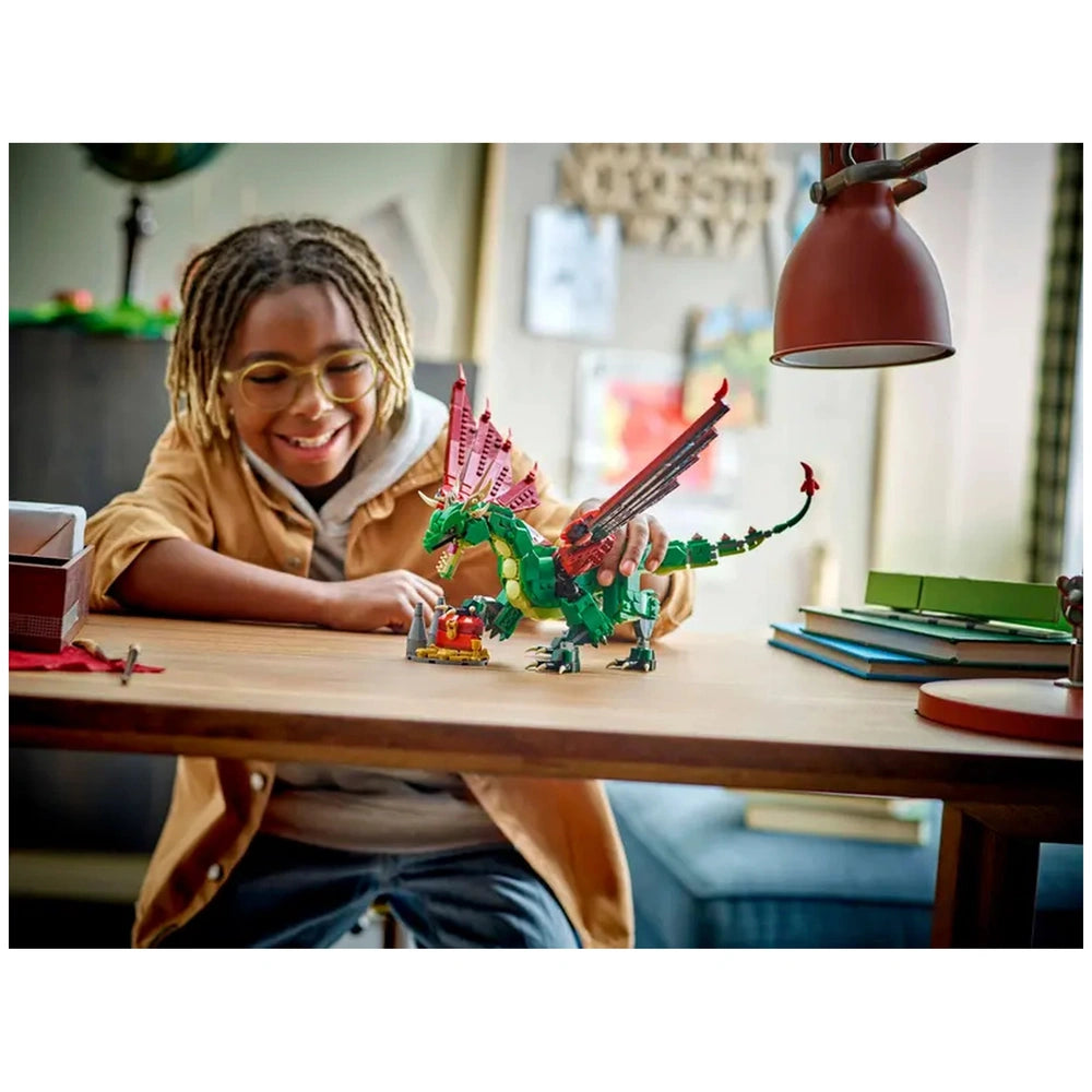 A smiling child with dreadlocks interacts with a colorful LEGO® Creator Medieval Dragon on a wooden table, surrounded by books and playful decor.