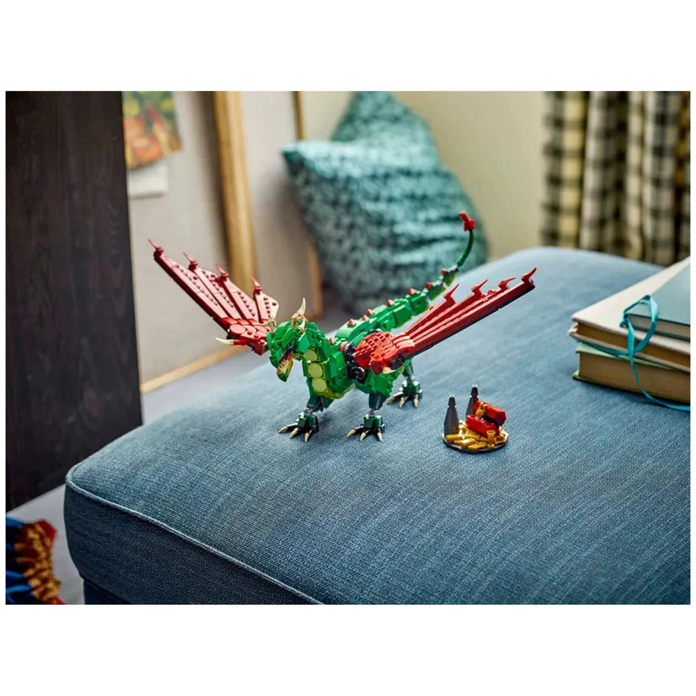 Green and red LEGO® Creator Medieval Dragon sits on a blue couch, featuring posable wings and intricate details, beside a small scene with figures and treasure.