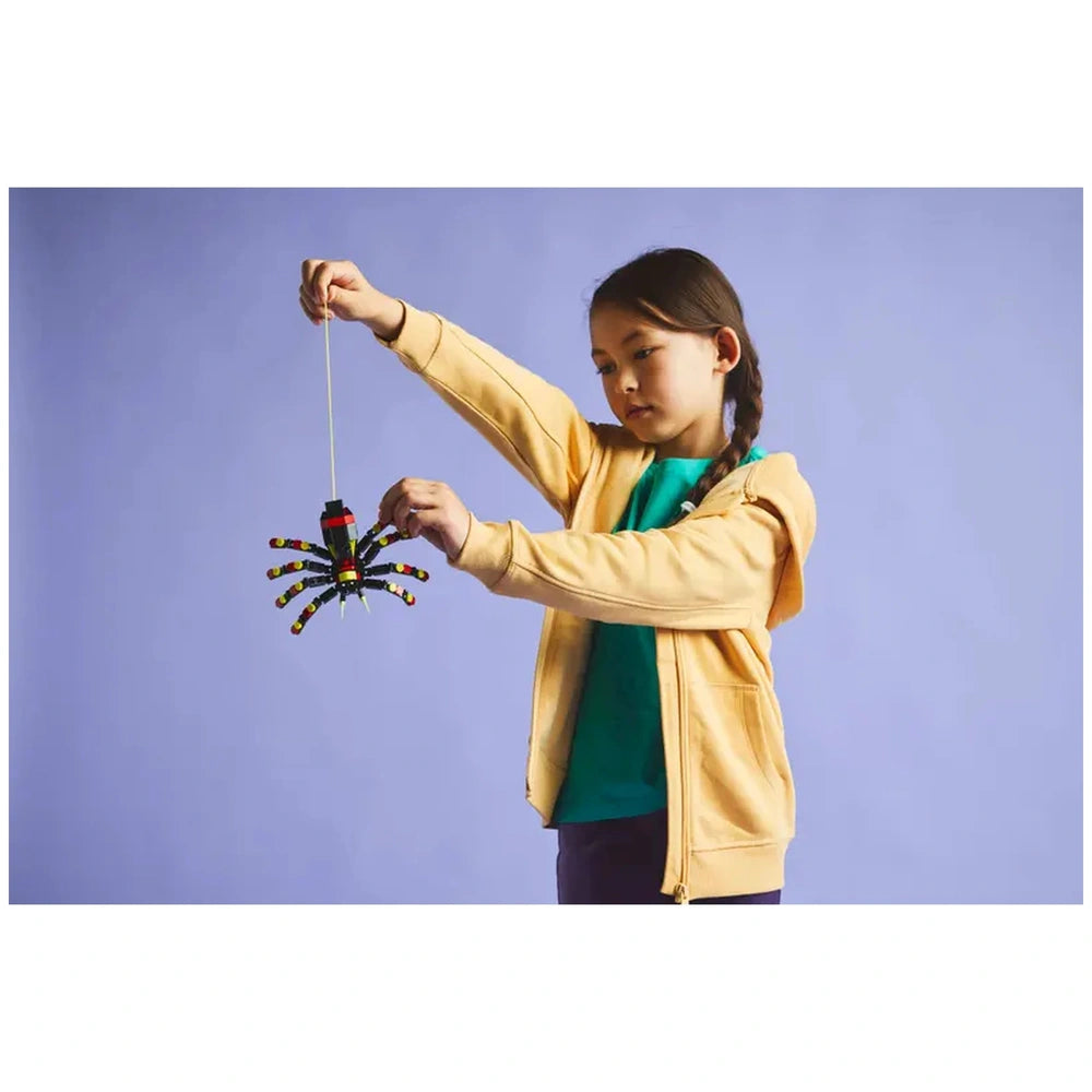 A child in a yellow hoodie holds a colorful LEGO Surprising Spider, showcasing its articulated legs and vibrant design against a soft purple background.