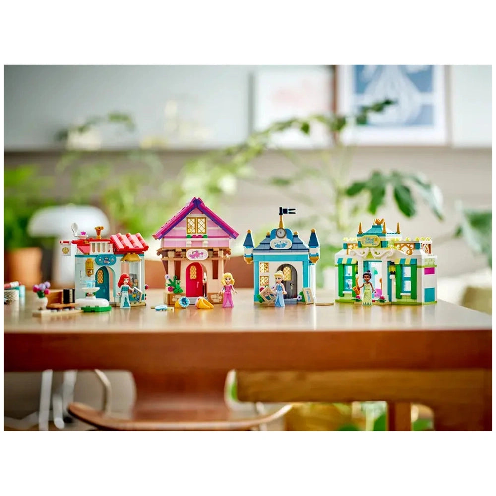 Colorful LEGO Disney Princess Market Adventure set featuring four detailed toy buildings, set on a wooden table, with characters nearby.