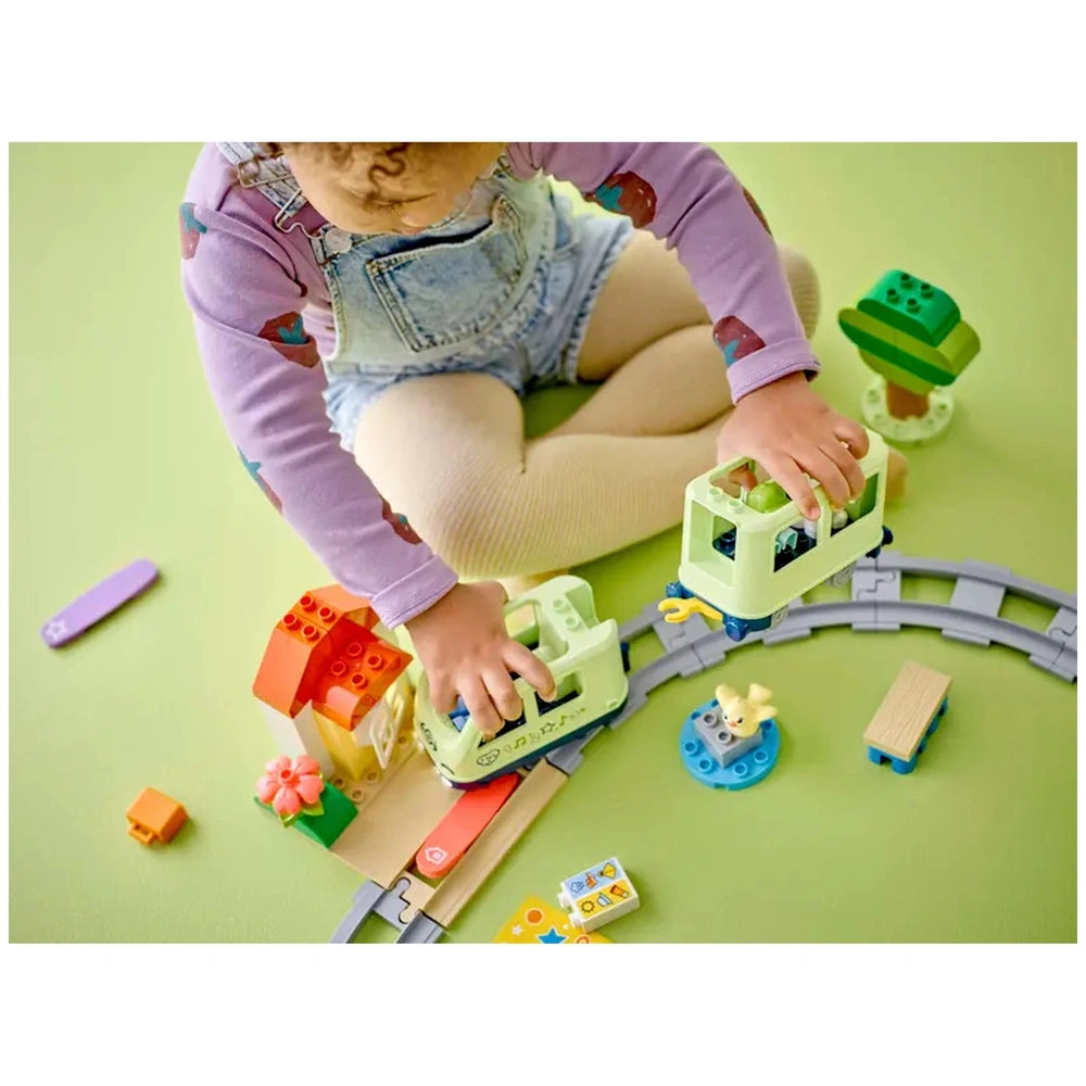 A child plays with the LEGO® DUPLO® Interactive Adventure Train set, assembling colorful blocks and trains on a soft green surface.