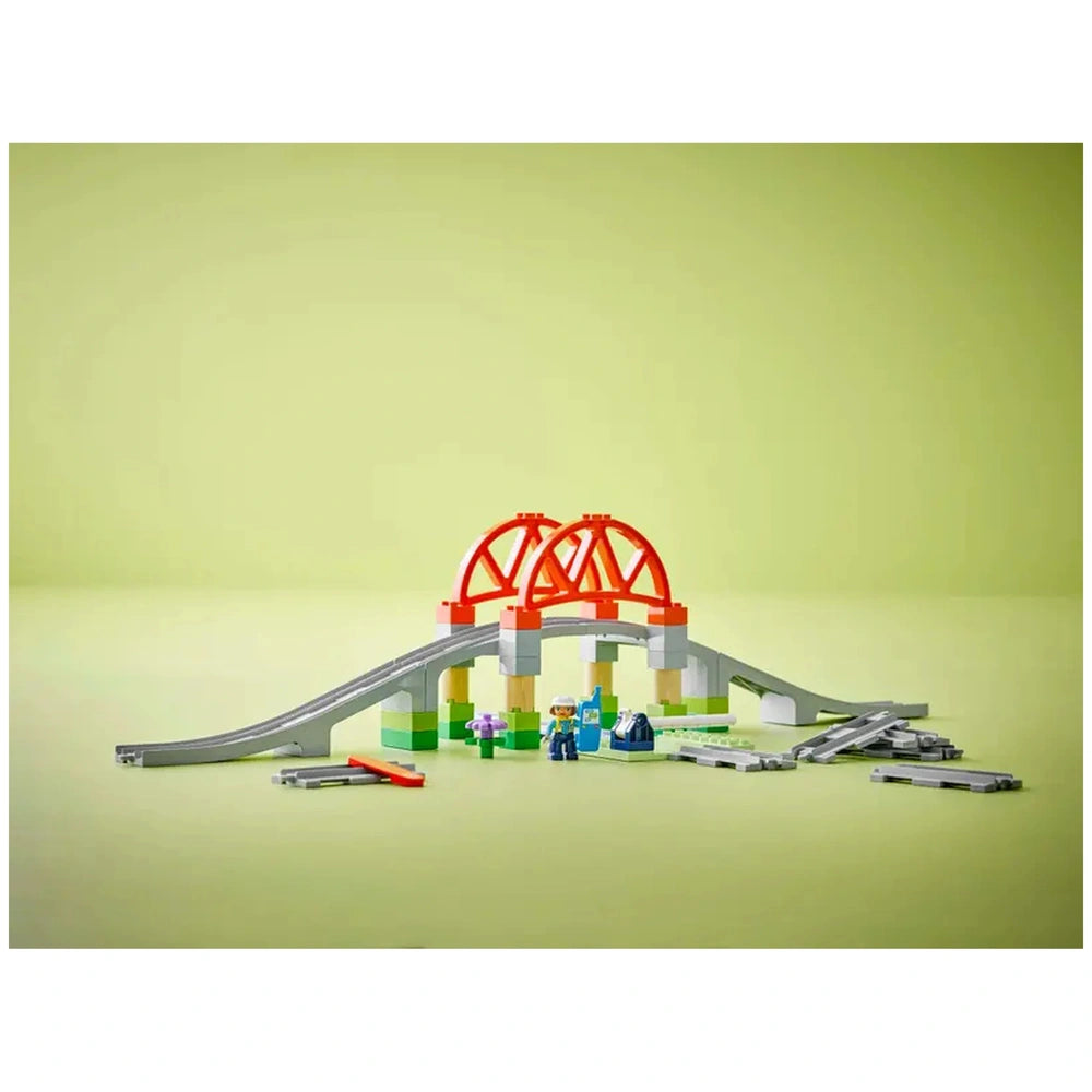LEGO® DUPLO® Train Bridge and Tracks Expansion Set featuring a colorful bridge, track pieces, and two mini figures on a light green background.