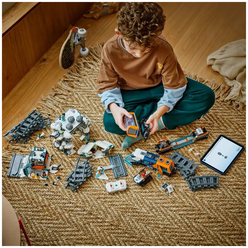 A child sits on a braided rug, focused on assembling the LEGO® Explorers’ Arctic Polar Express Train set with various pieces scattered around. An illustrated instructions tablet lies nearby, showcasing construction steps.