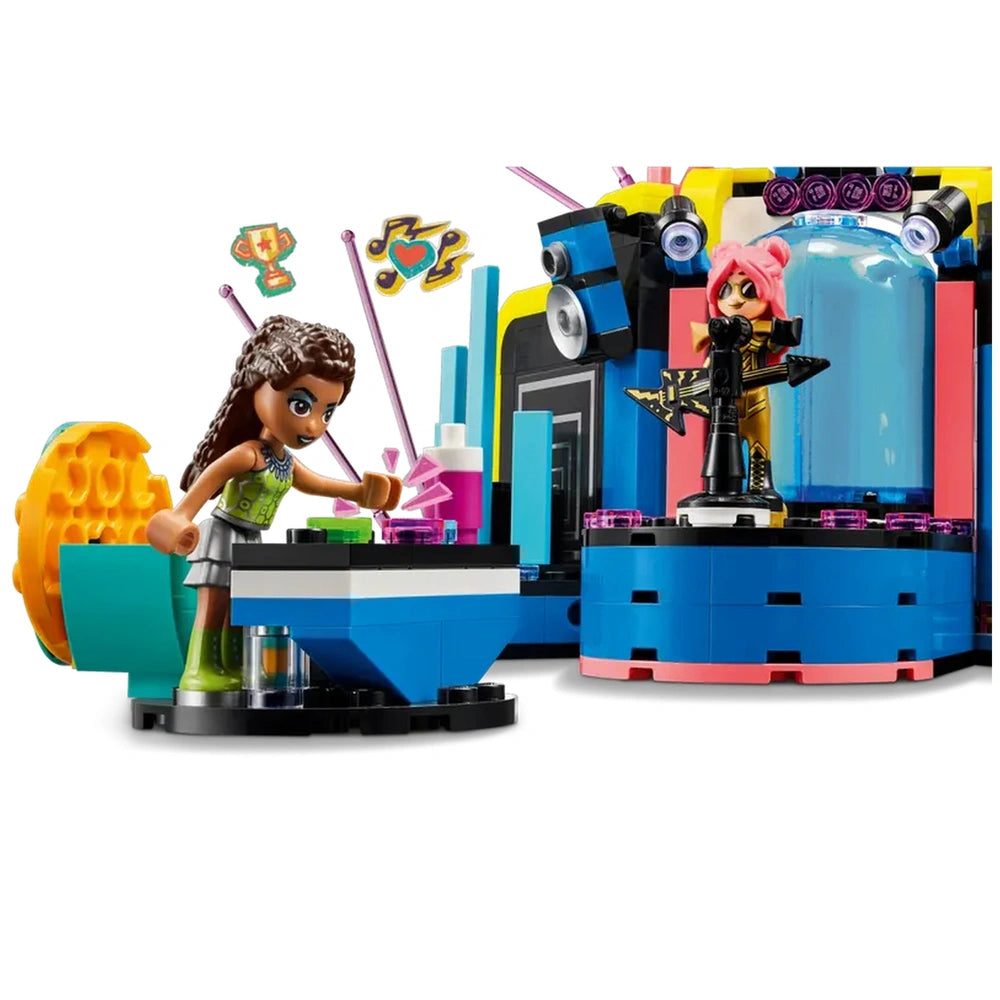 Two mini-dolls perform on a colorful LEGO music stage, with one playing keyboard and the other singing into a microphone, surrounded by musical notes and lights.