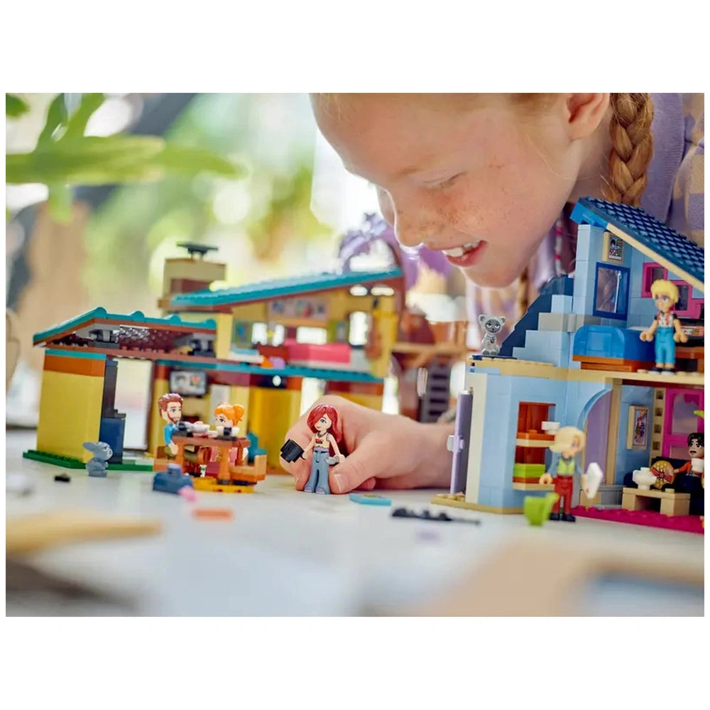 A child joyfully plays with the LEGO Friends Olly and Paisley's Family Houses set, featuring two colorful houses and mini-dolls.