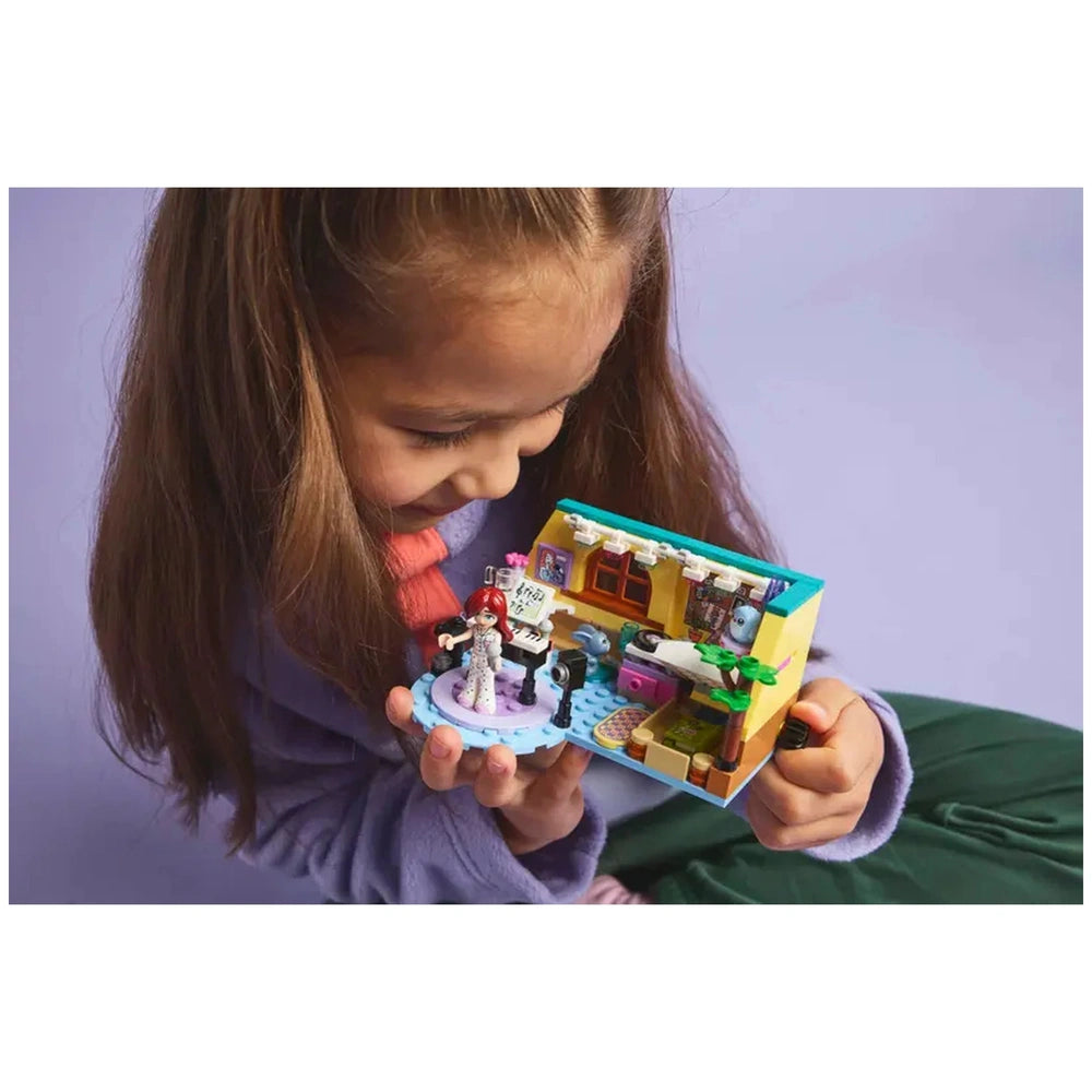 A young girl smiles while holding the LEGO® Friends Paisley’s Room construction set, featuring colorful details and two minidolls.