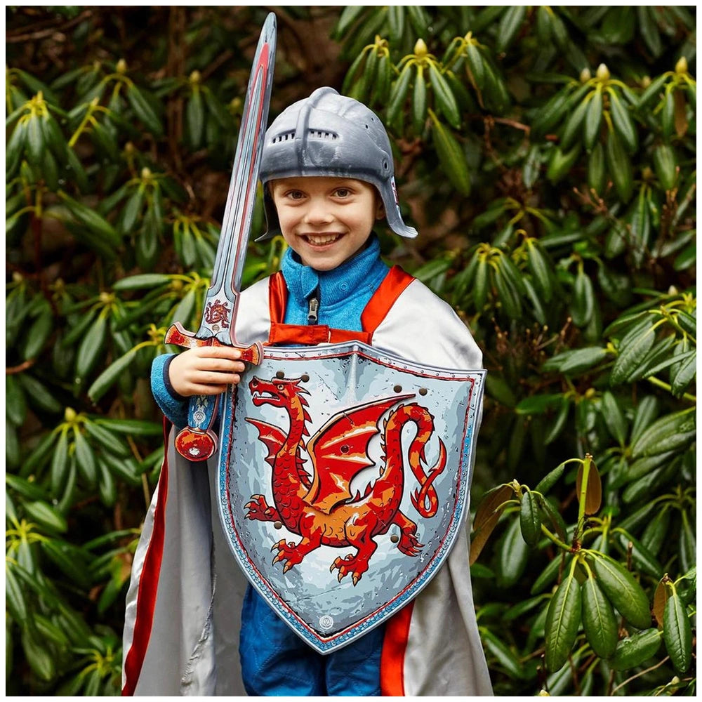 Liontouch Amber Dragon Cape worn by a child with a silver helmet, red dragon shield, and sword, set against green foliage.