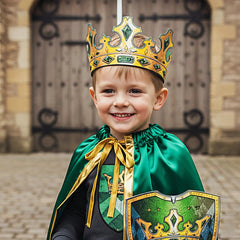 Child wearing a green velvet cape and gold crown holds a green and blue shield in front of a wooden door.