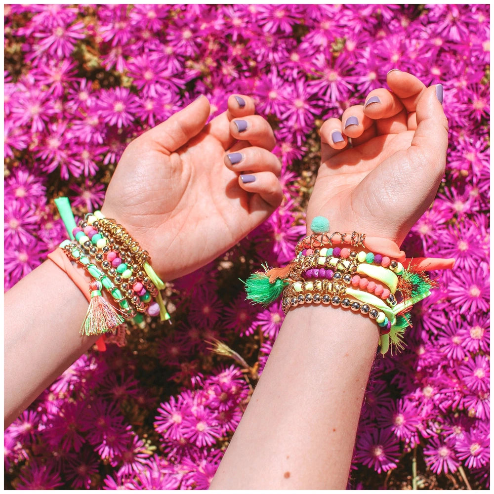Neo-Brite Chains and Charms displayed with two hands adorned with purple fingernails and purple flowers in the background.