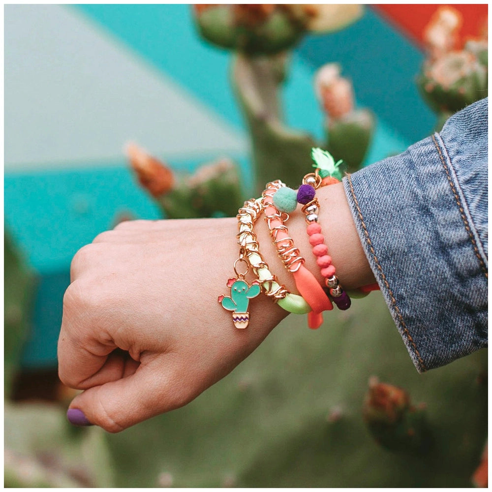 Colorful Neo-Brite bracelets adorn a person's hand, with a green cactus providing a vibrant background.
