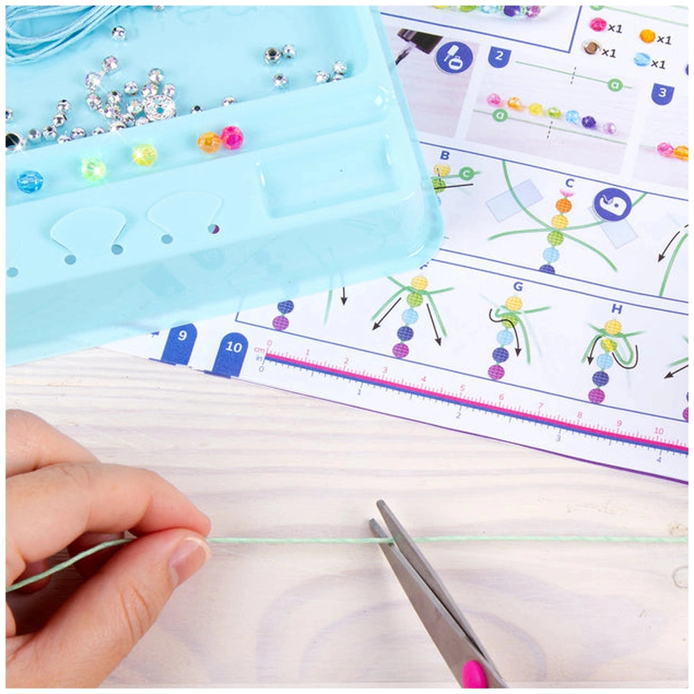 Rainbow Bling Bracelets kit featuring a blue container, clear lid, white patterned paper, green string, and pink scissors.