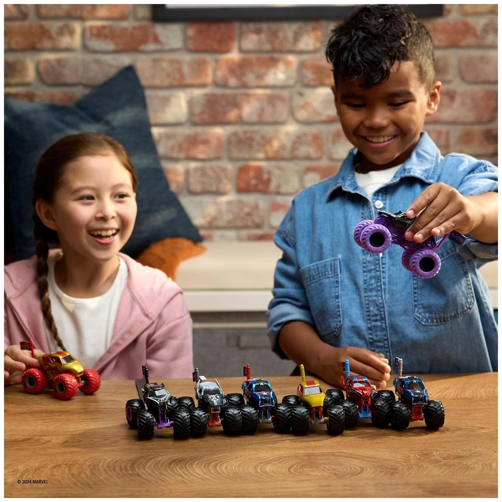 Marvel Monster Jam Truck toy figures are being played with by a smiling girl and a boy at a wooden table.