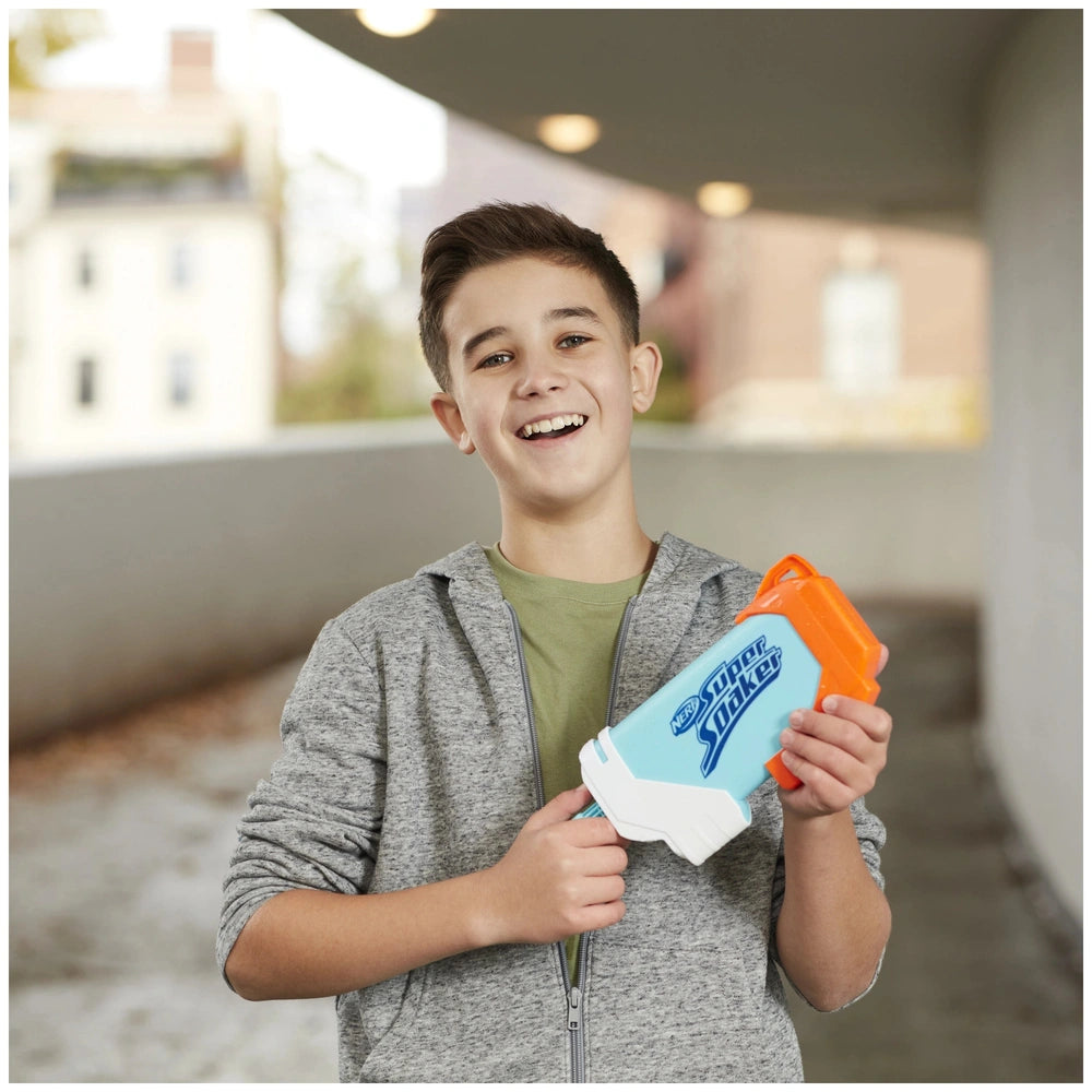 Nerf Super Soaker Torrent Water Blaster held by a smiling boy in a gray sweatshirt against a concrete wall.