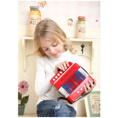 Red accordion held by a young girl in a white shirt and blue jeans, surrounded by decorative jars and plants on a shelf.