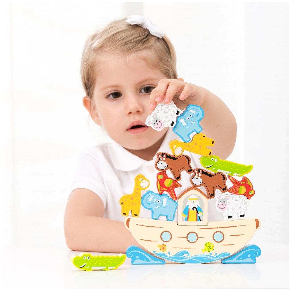 Young girl in a white shirt holding a toy boat with colorful animals, featuring a brown base and white top on a white tableto