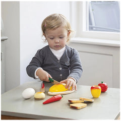 New Classic Toys breakfast box set features a child playing with colorful plastic food and utensils on a wooden table.