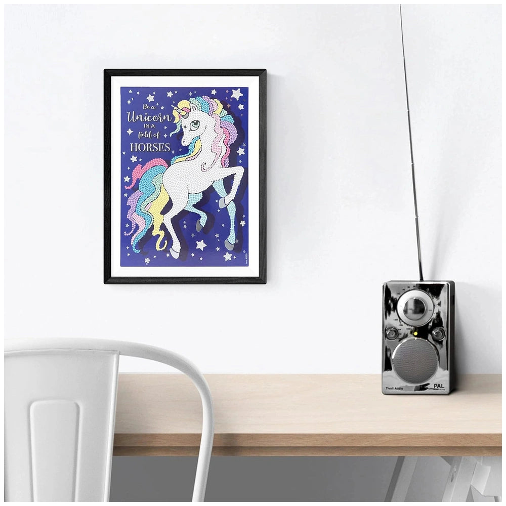 Diamantiny Crystal Art Design Set displayed on a wooden table with a glossy unicorn picture and a silver and black radio.
