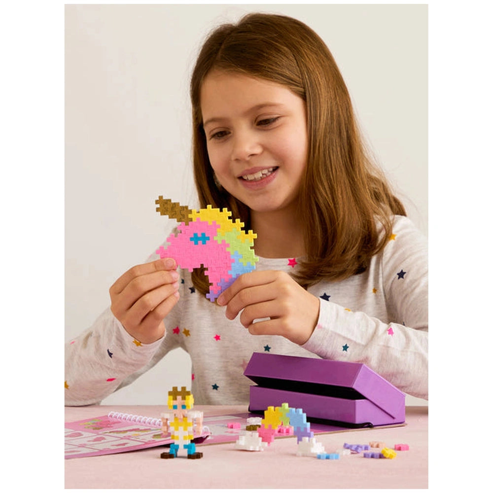 Young girl in star-patterned top engages with Plus Plus Fairytale Activity Pad, surrounded by Lego unicorn, castle, and scatt
