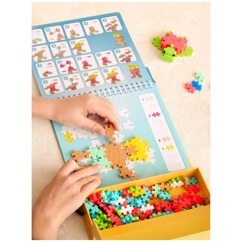 Plus Plus Ocean Activity Pad with blue cover, puzzle pieces in yellow container, and a hand holding a colorful piece.