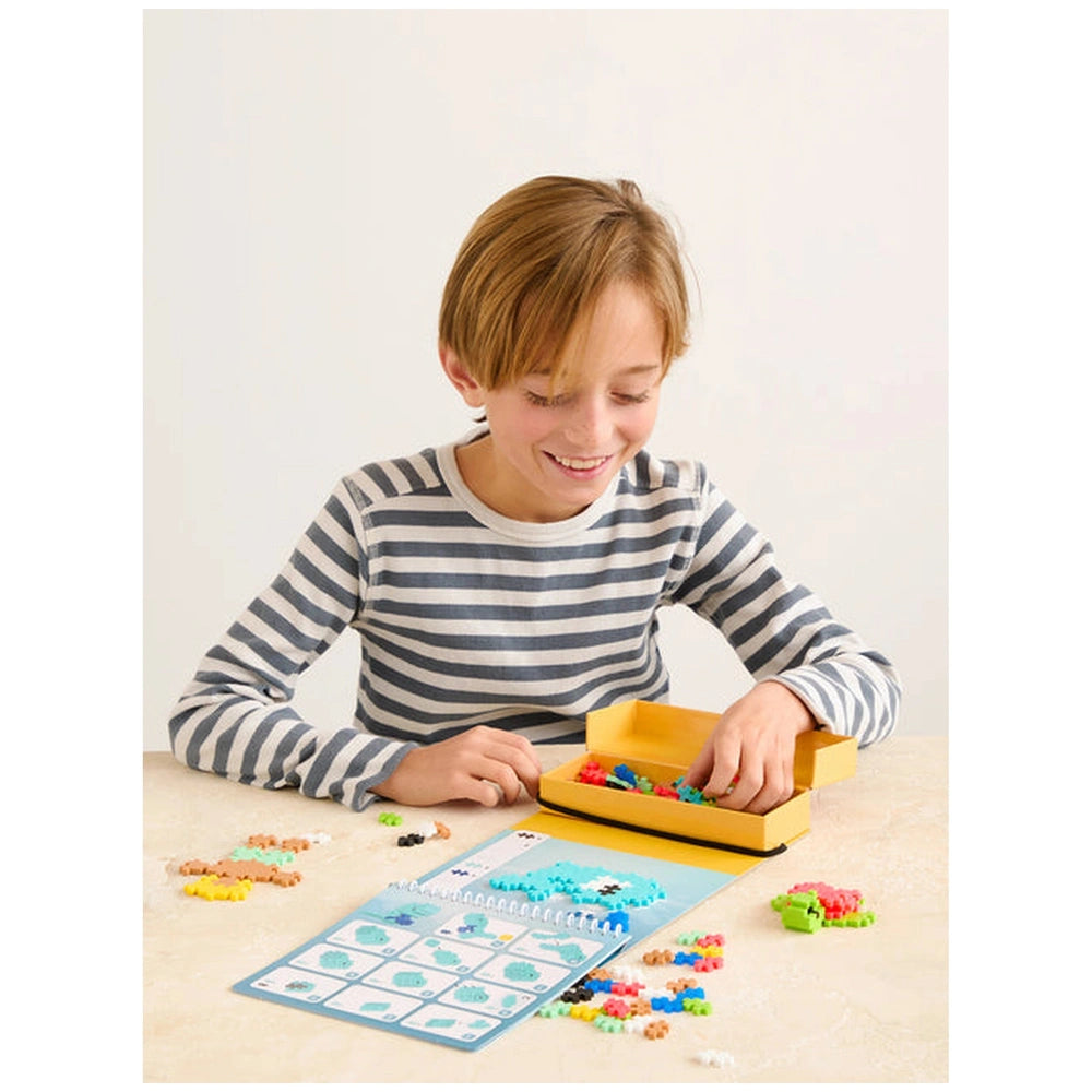 Plus Plus Ocean Activity Pad with colorful beads on a light table, held by a smiling young person in a striped shirt.