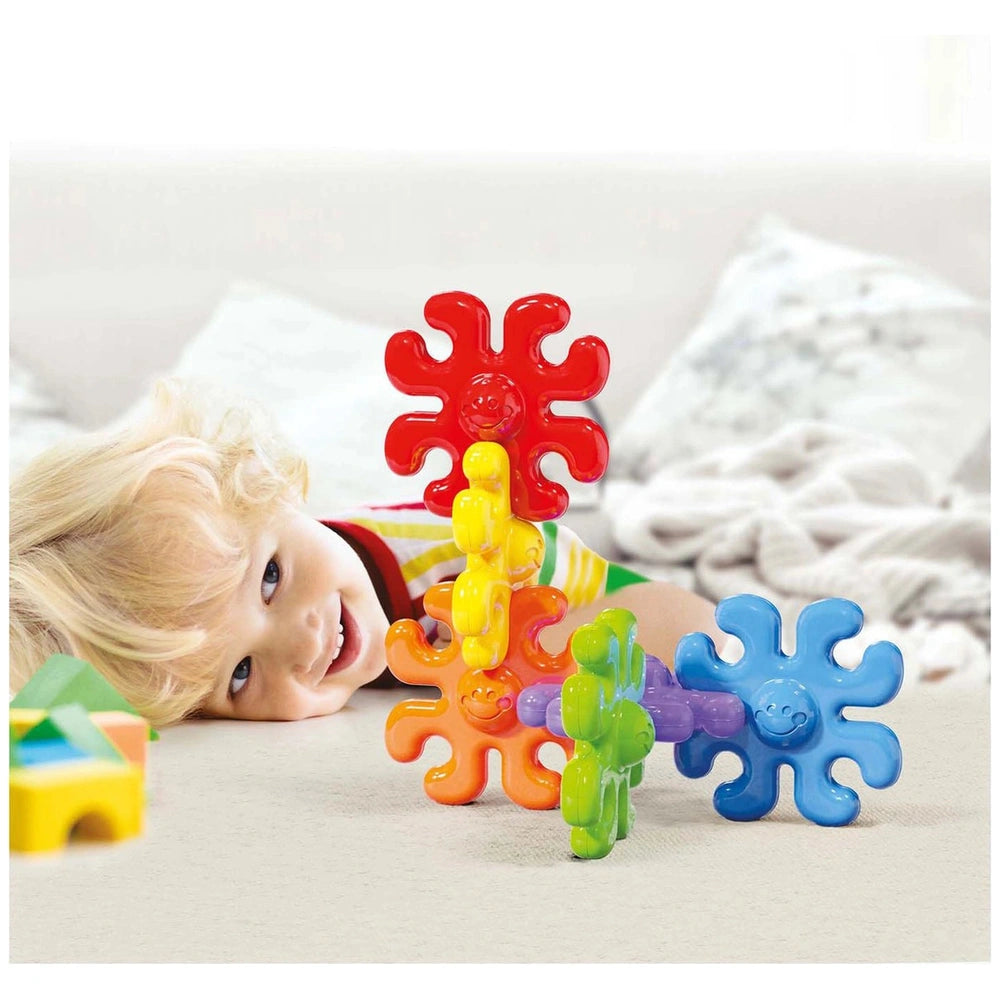 Quercetti Polipetti baby activity toy being enjoyed by a smiling child with blonde hair, dressed in a colorful striped shirt.