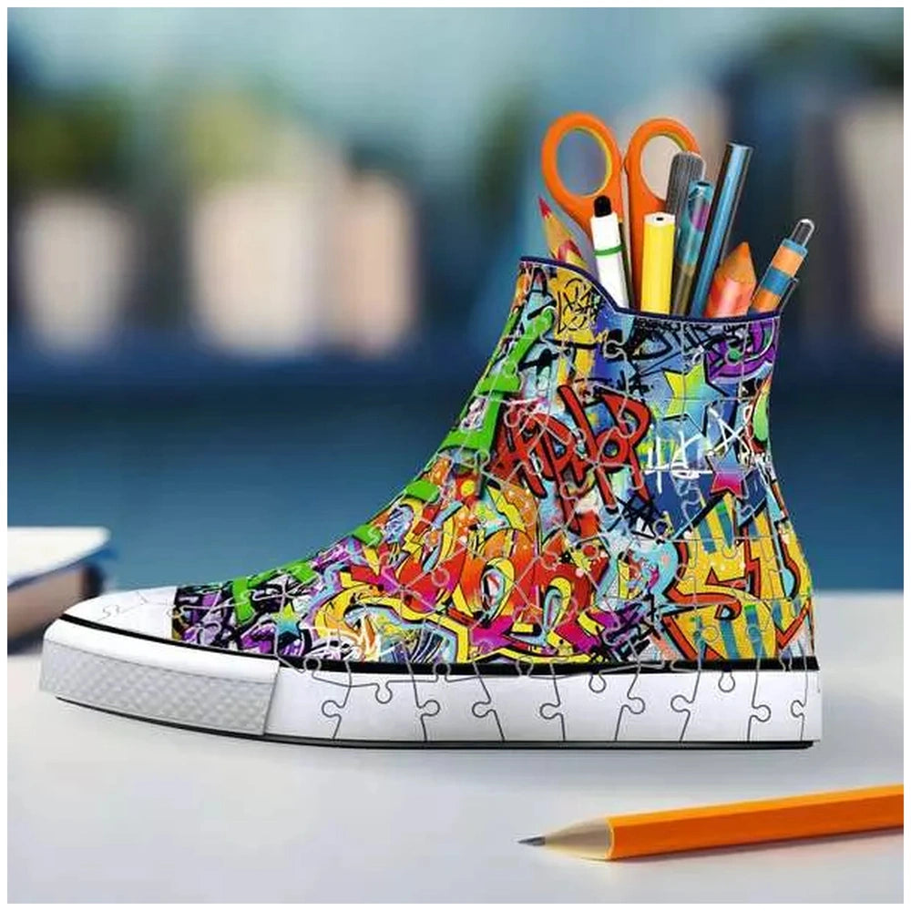 Colorful graffiti-style sneaker with writing instruments in an attached container, set against a blurred outdoor background.