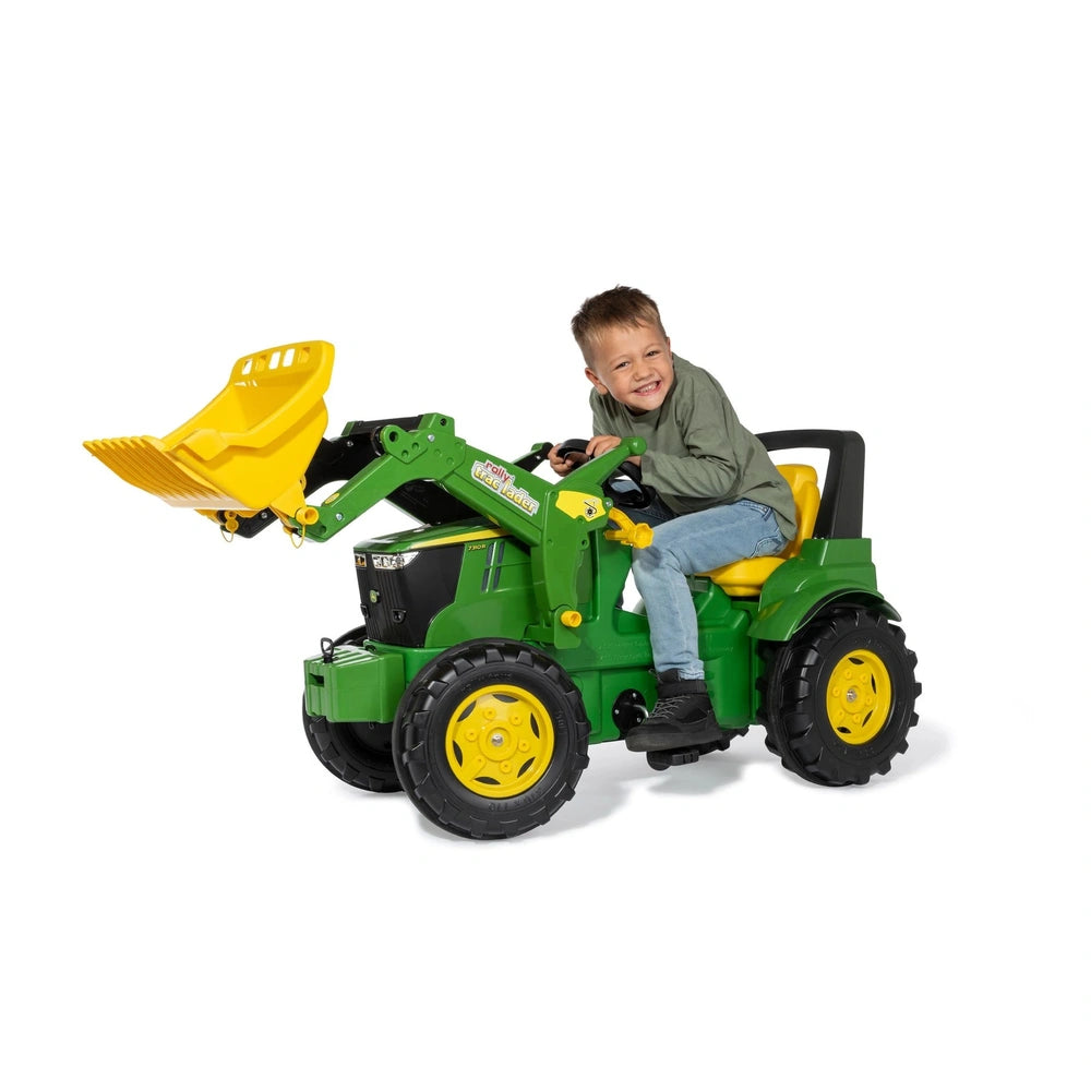Rollyfarmtrac John Deere 7310R toy tractor with a smiling child in a green shirt and blue jeans, featuring a yellow bucket at