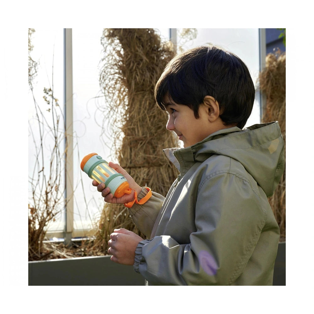 Scout 2-in-1 Kids Flashlight held by a smiling child outdoors, wearing a green jacket, with a greenhouse in the background.