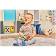 Simba - ABC First Rattle - A smiling child on a carpet holds a colorful rattle amidst a vibrant playroom filled with toys.