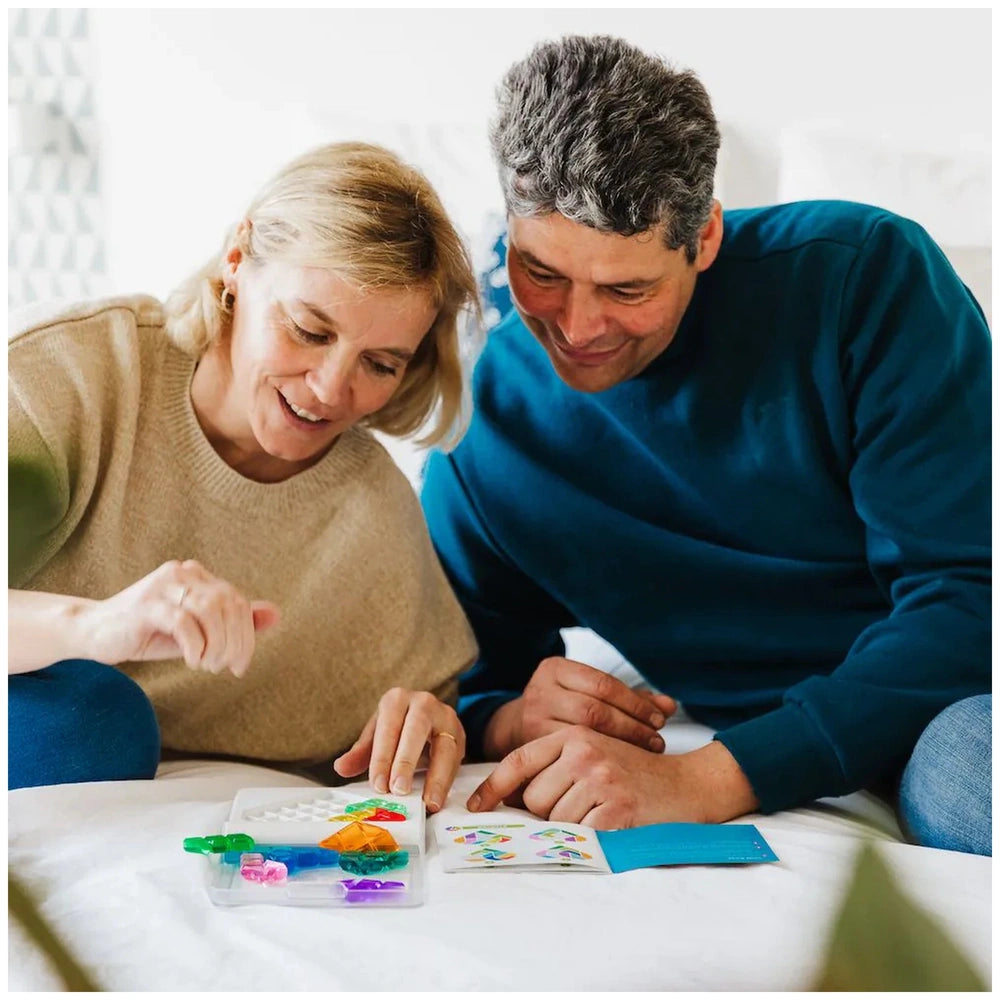 Smart Games IQ Love logic puzzles are being explored by a man and woman sitting on a bed, focused on a colorful object.