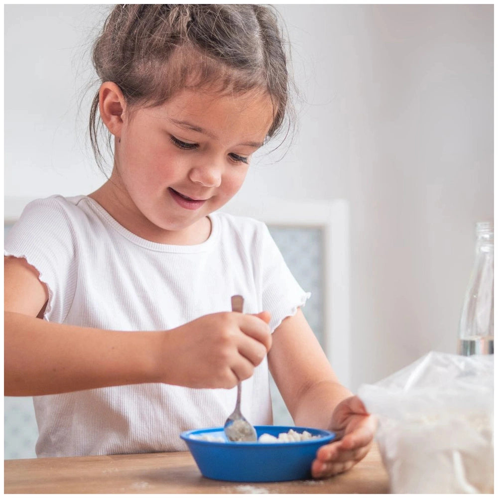 Teifoc accessory set features a young girl smiling while scooping food from a blue bowl on a wooden kitchen surface.