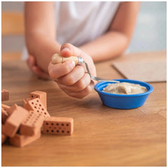 Teifoc water mill set displayed on a wooden surface, with a child’s hands holding a wooden mallet and various craft objects.